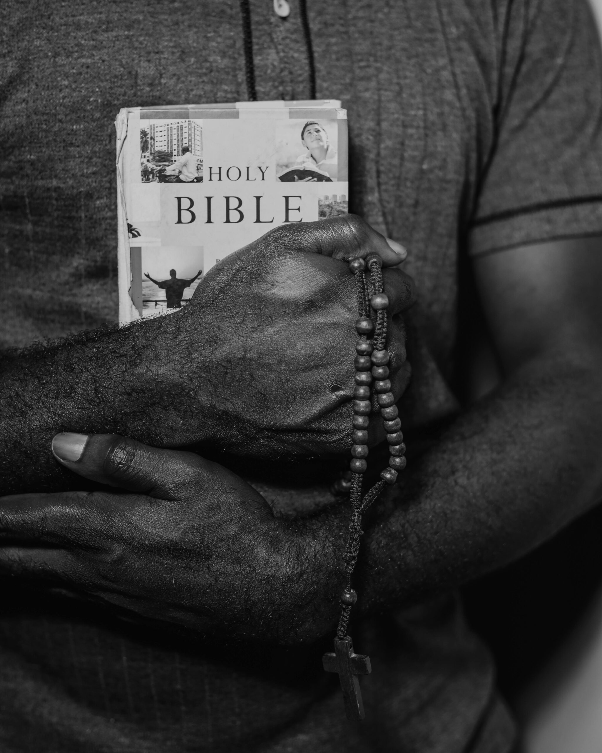 Black and white photo of hands holding a Bible and rosary beads, symbolizing faith.